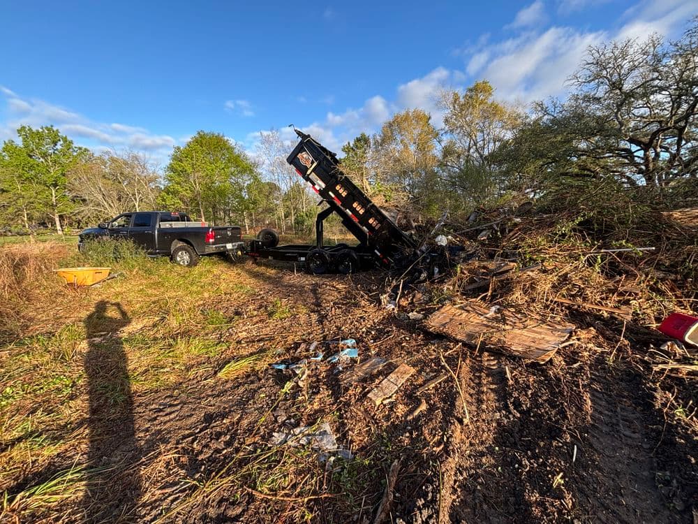 Truck with trailer tipped over in a wooded area, surrounded by debris and fallen branches.
