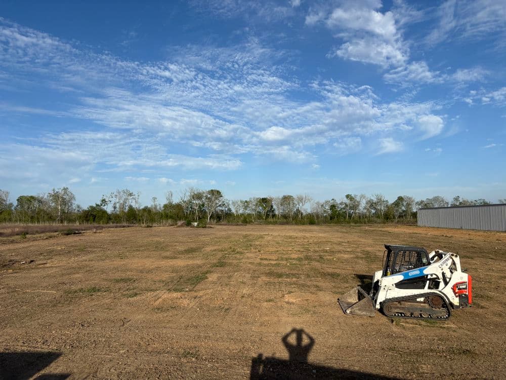 Cleared land with a skid steer loader under a blue sky and scattered clouds.