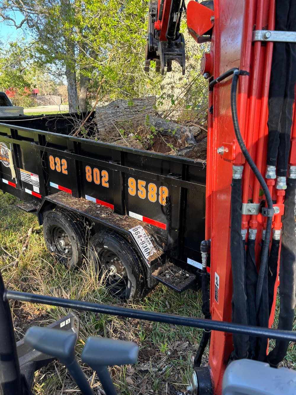 Construction equipment unloading debris into a black dump trailer on a green landscape.