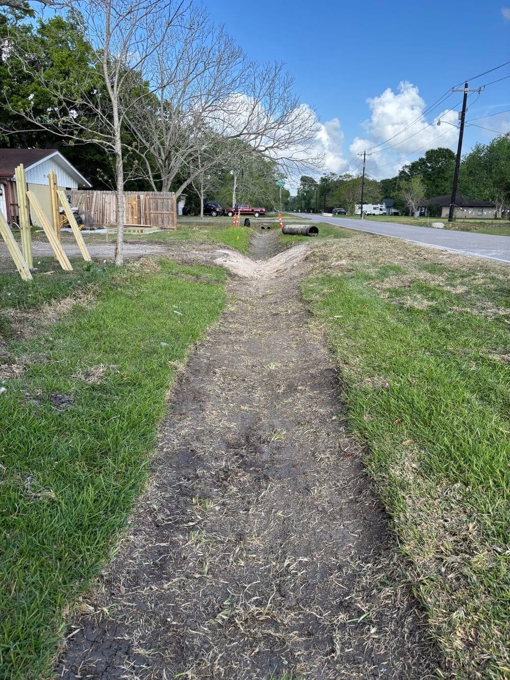 Diverging drainage ditch in a residential area with grassy edges and blue sky.