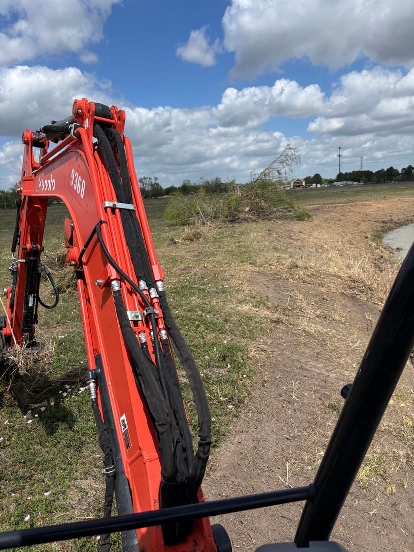 Red excavator on a grassy field with cloudy skies and distant trees. Construction equipment in use.