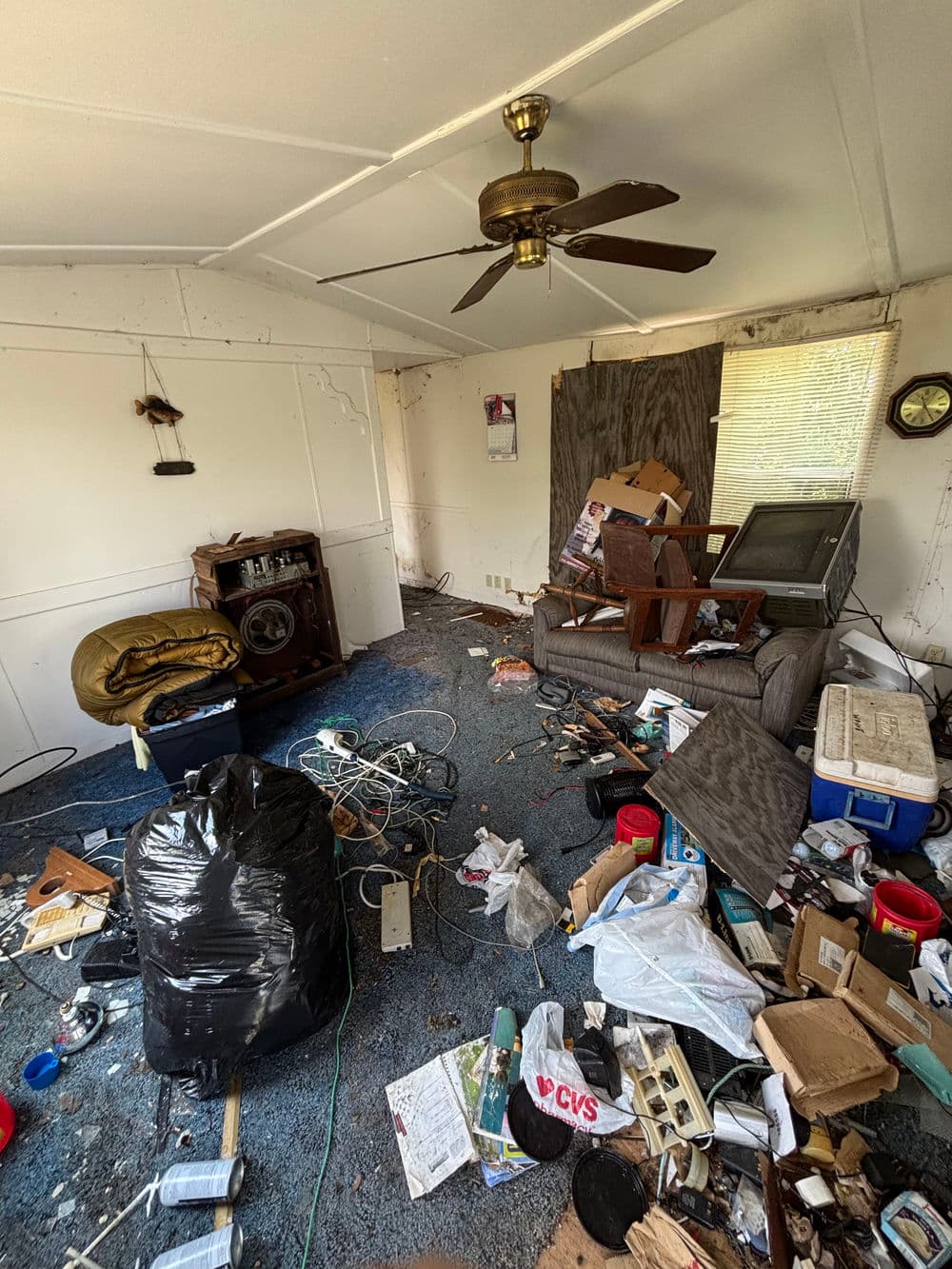 Cluttered living room with trash, debris, and disorganized furniture, showing neglect and disarray.