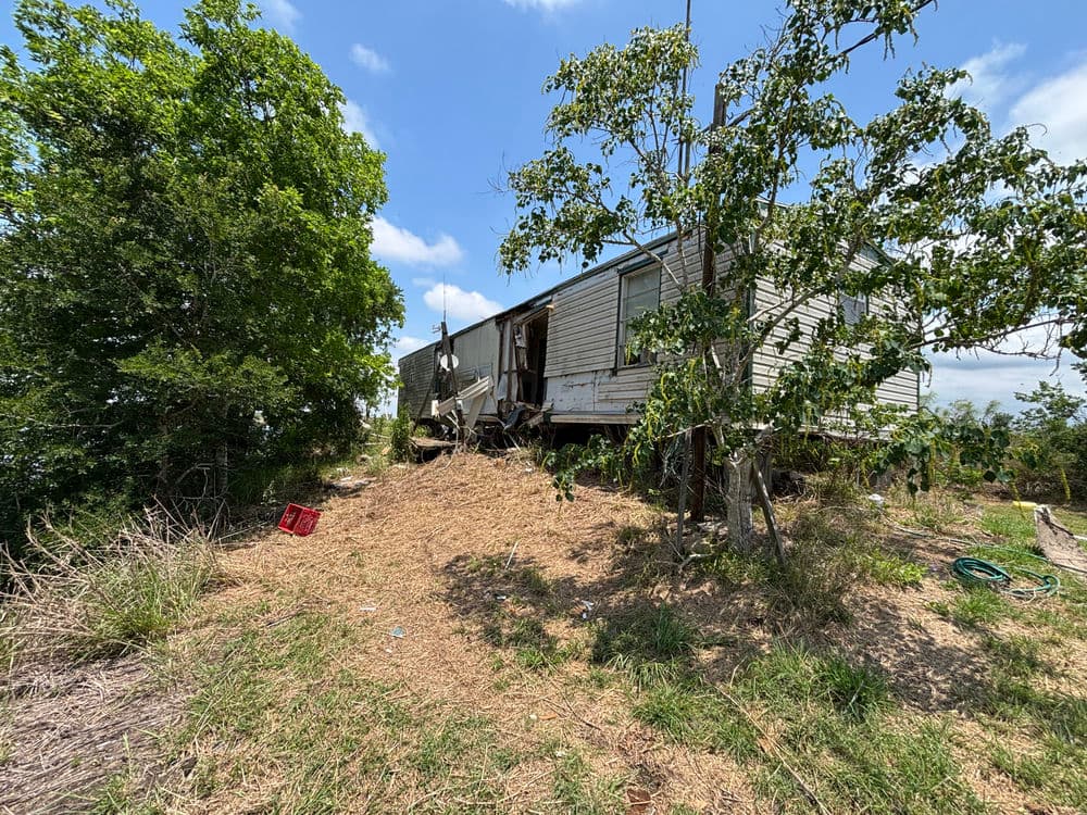 Abandoned mobile home on a hillside surrounded by overgrown vegetation and trees.