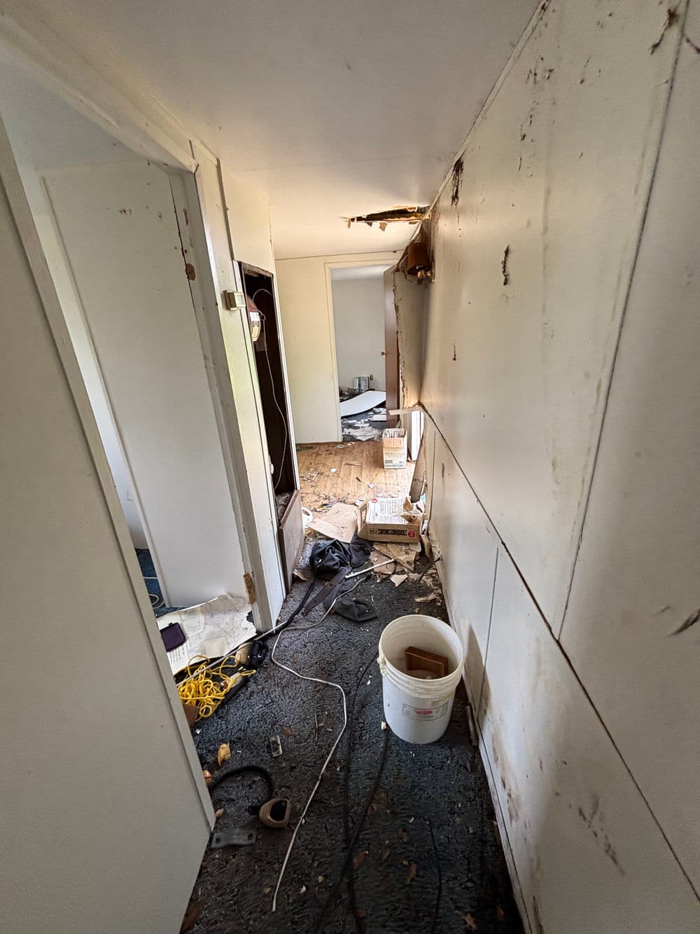 Renovation project in a hallway with exposed walls, debris, and tools scattered on the floor.