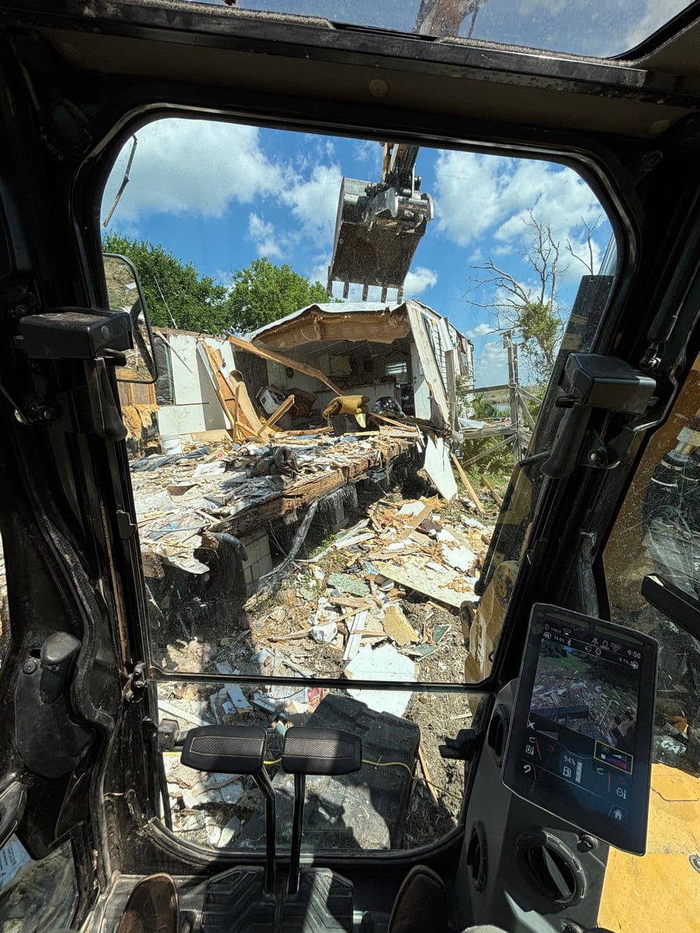View from inside an excavator cab, showcasing a building demolition in progress.