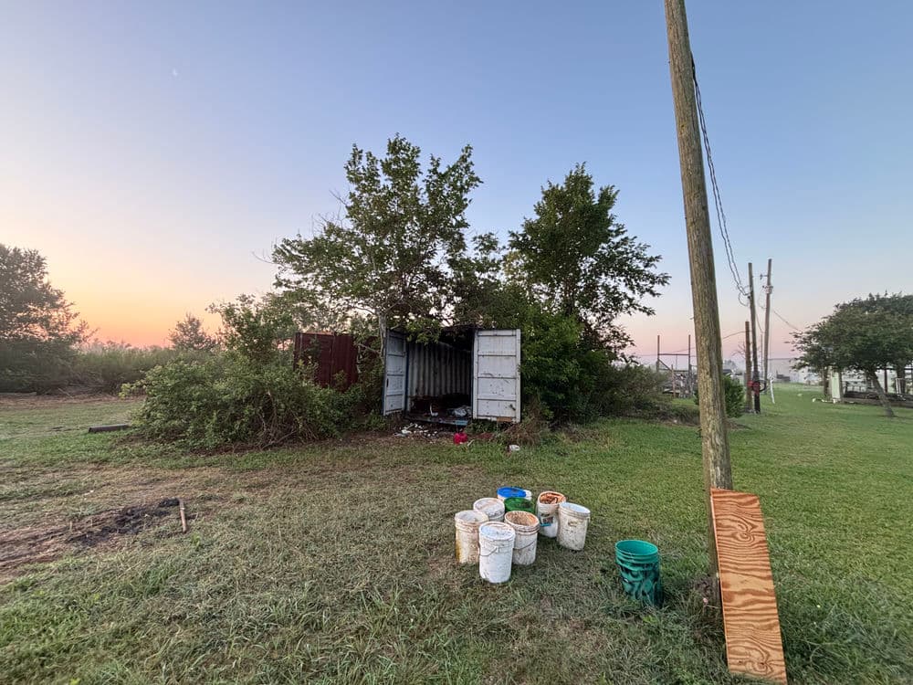 Abandoned container storage with buckets on grassy lot at sunrise.
