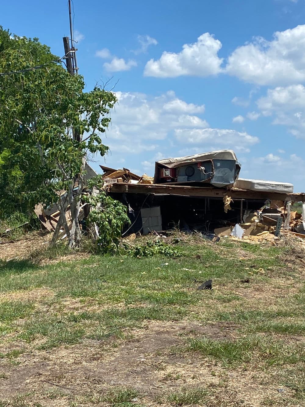 Damaged structure with debris, toppled trailer, and a blue sky in the background.
