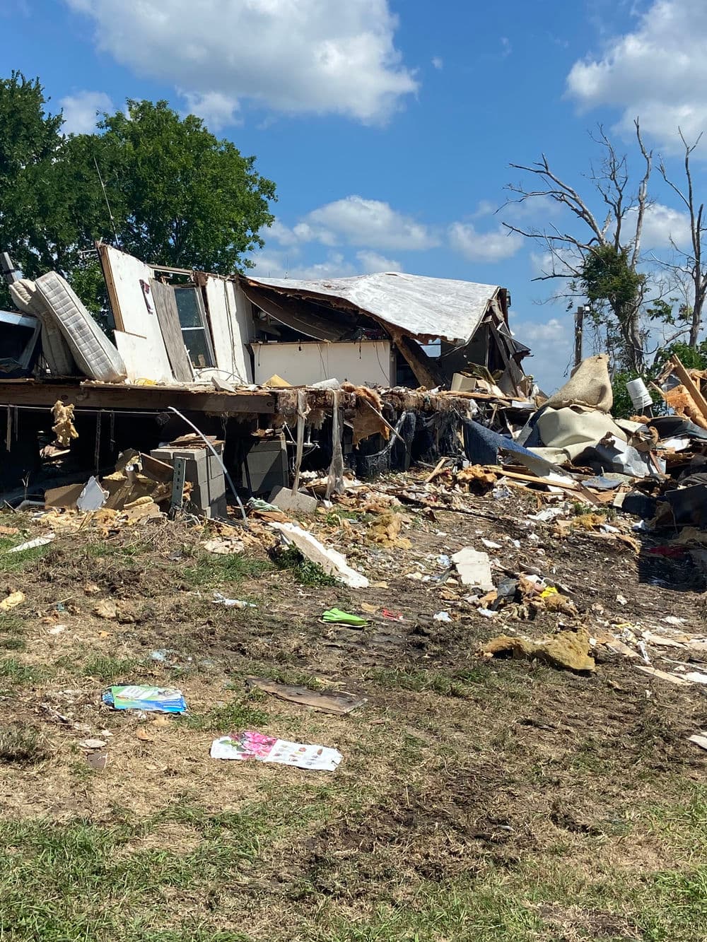Severely damaged house debris scattered on the ground after a natural disaster.
