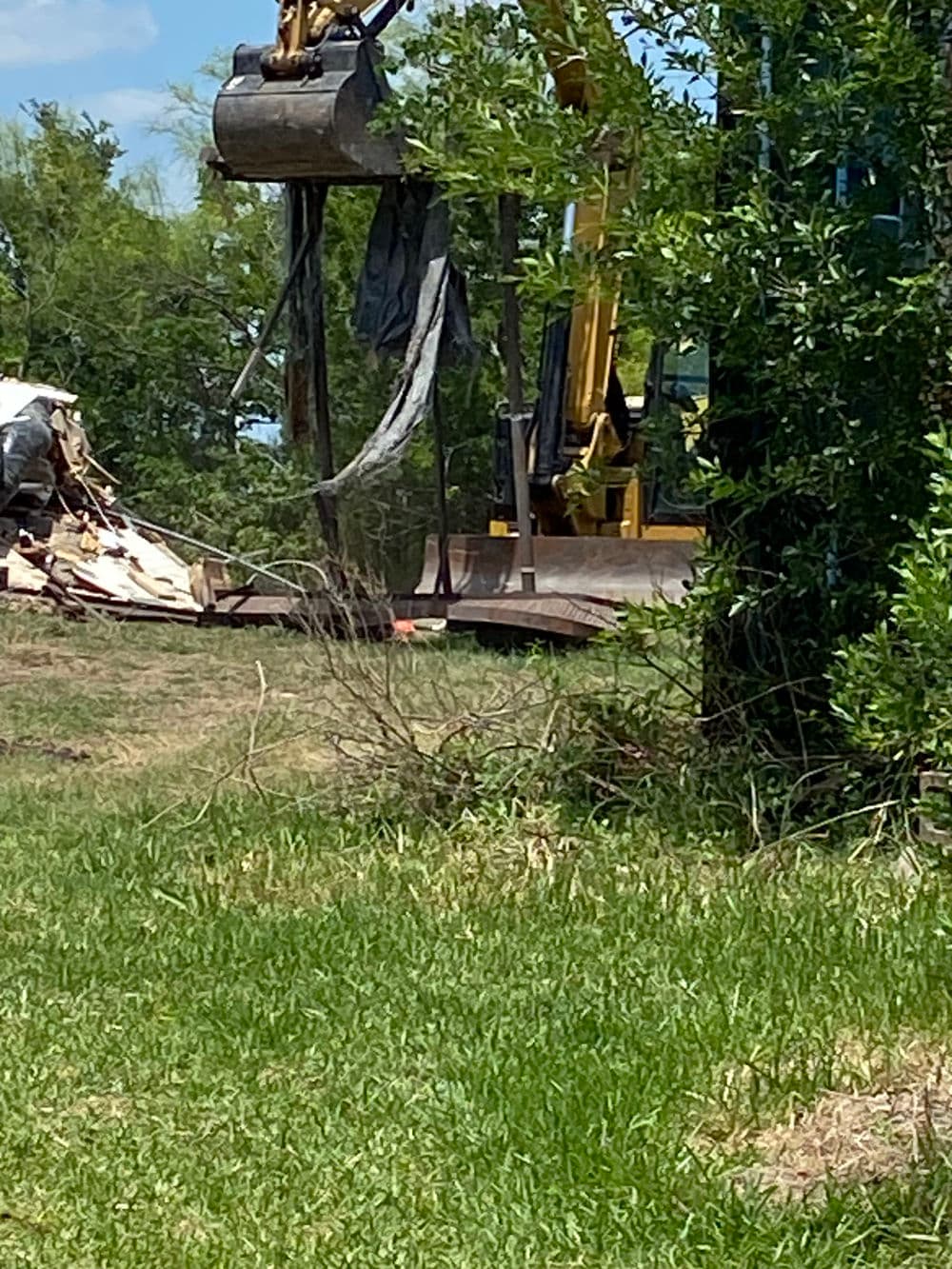 Excavator working on demolition site with debris and greenery in the background.