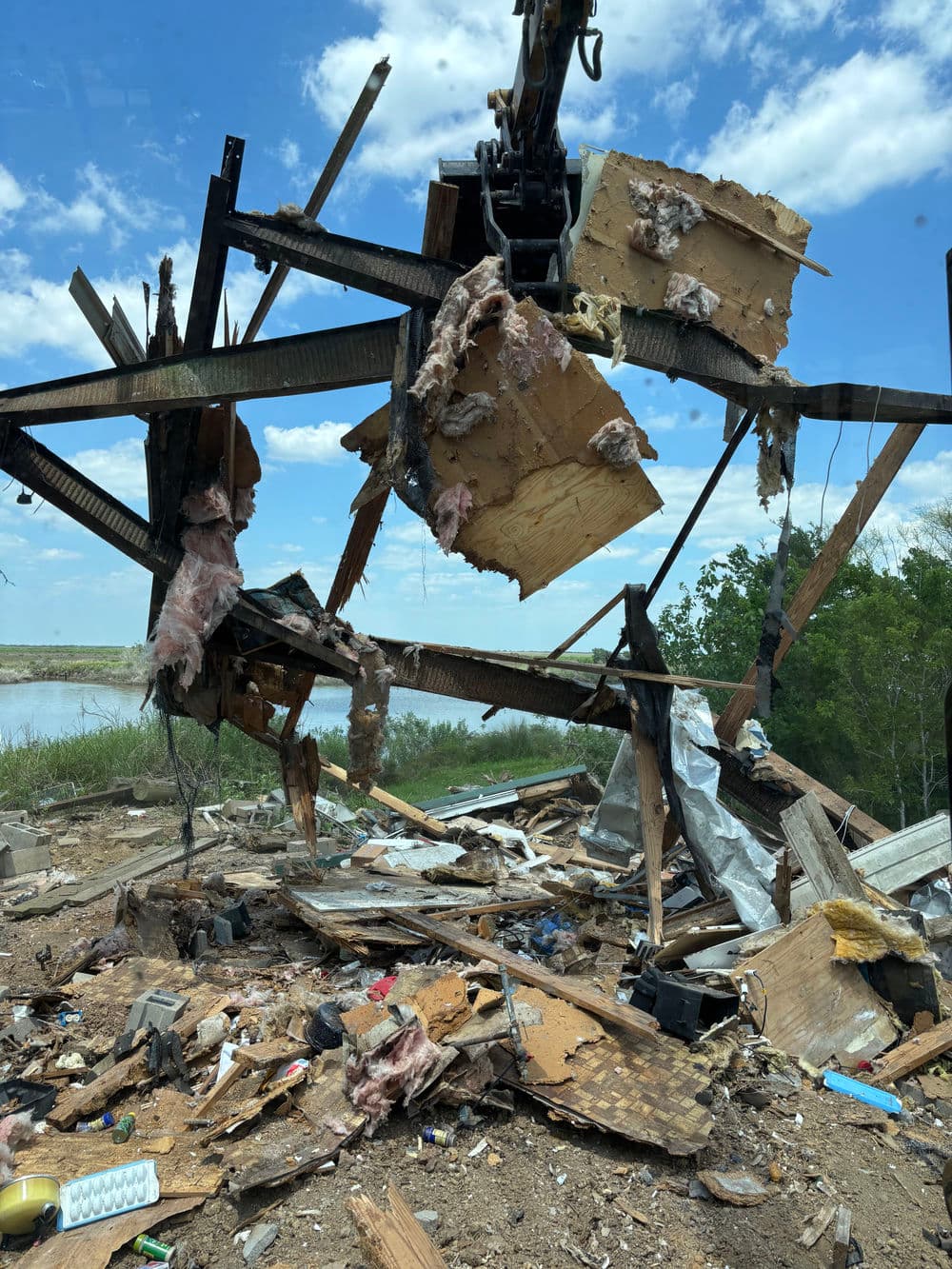 Demolition scene with debris, metal beams, and insulation against a blue sky and lake backdrop.
