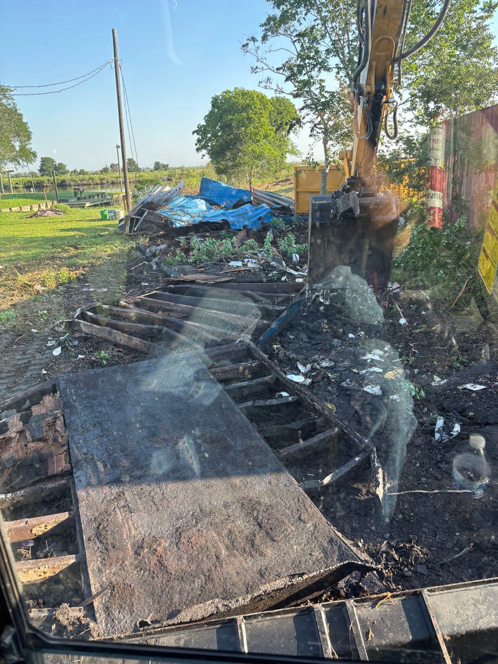 Excavator clearing debris in a landscape with scattered construction materials.