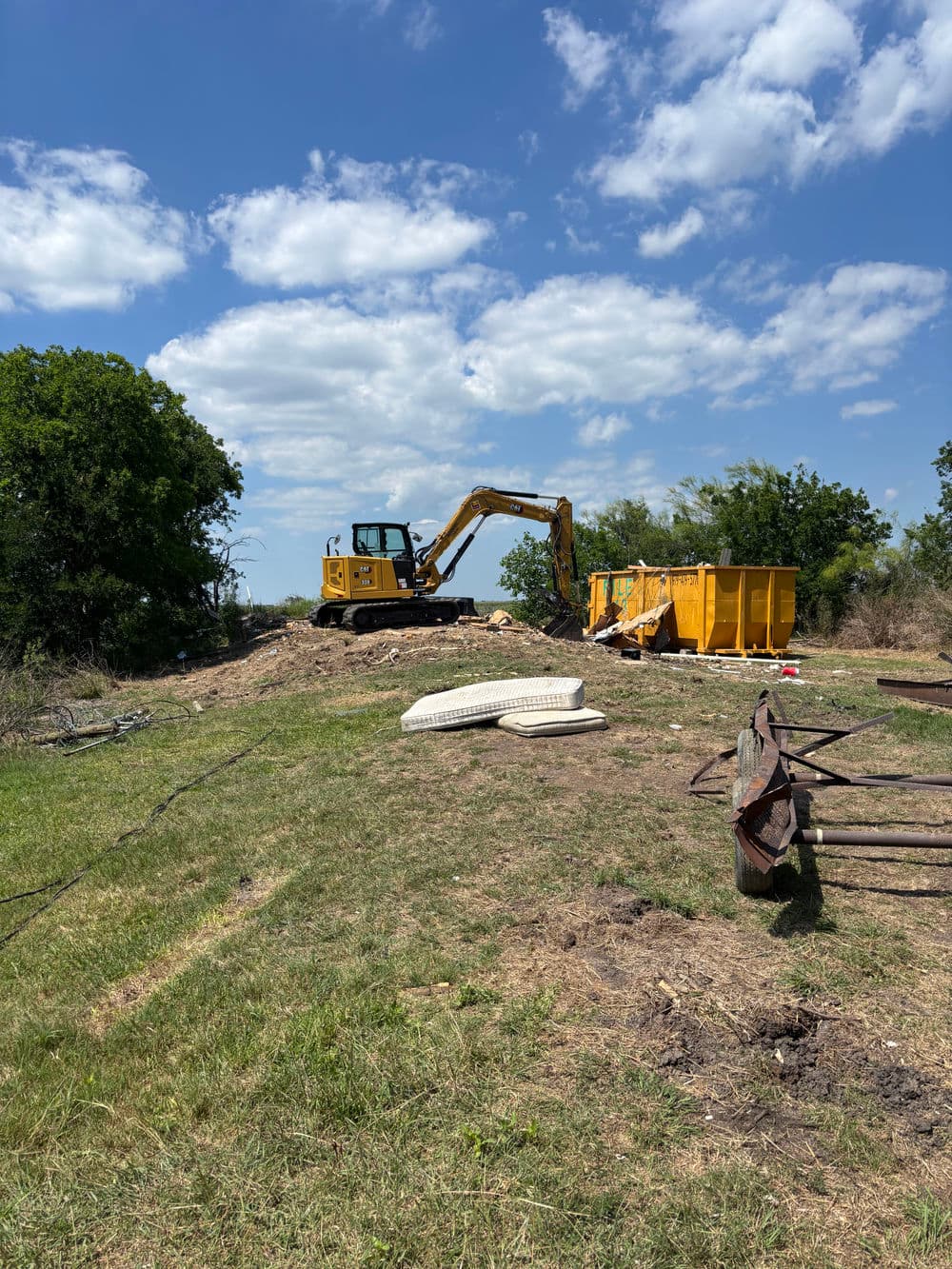 Excavator working on a construction site with a waste container and grassy terrain.