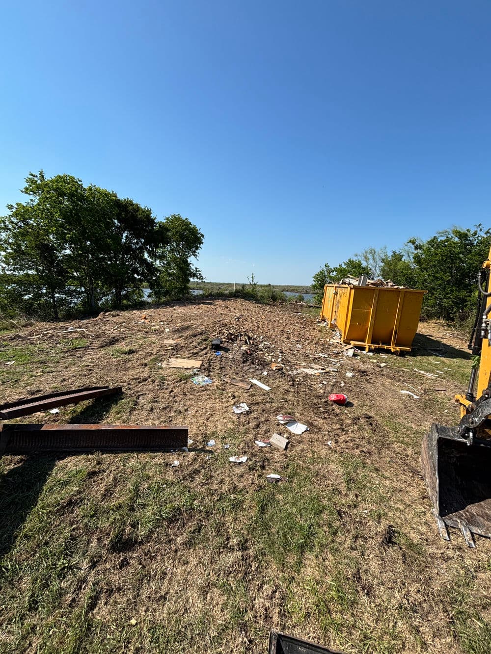 Littered landscape with yellow dumpsters and debris under a clear blue sky.