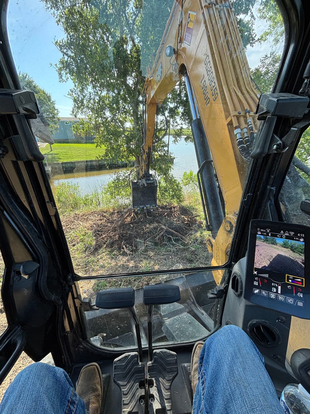 View from excavator cab overlooking a riverbank with tree removal in progress.