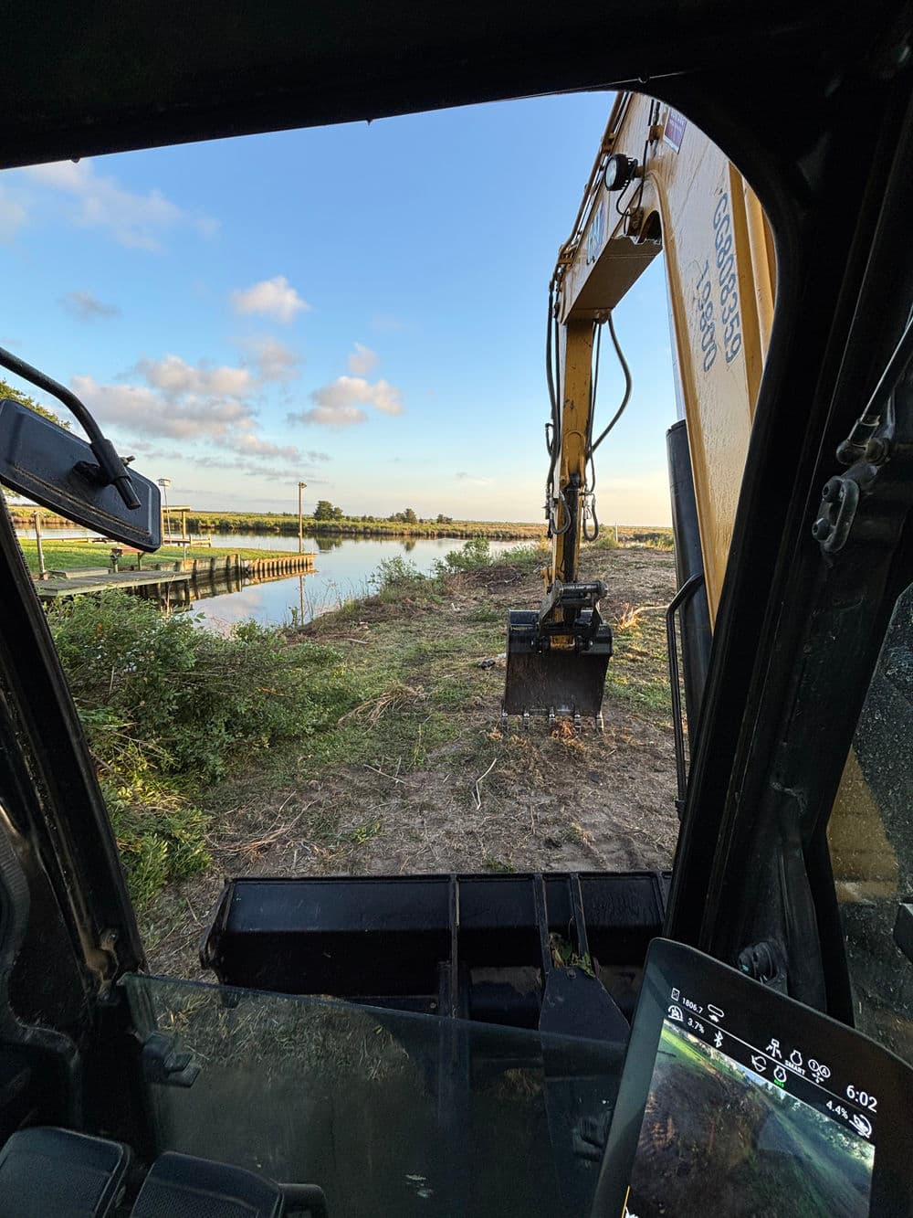 Excavator working near water, viewed from inside the machine’s cabin at sunset.