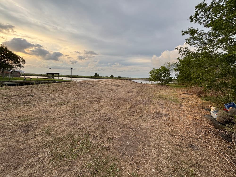Sunset over a cleared riverbank with sparse vegetation and distant water view.