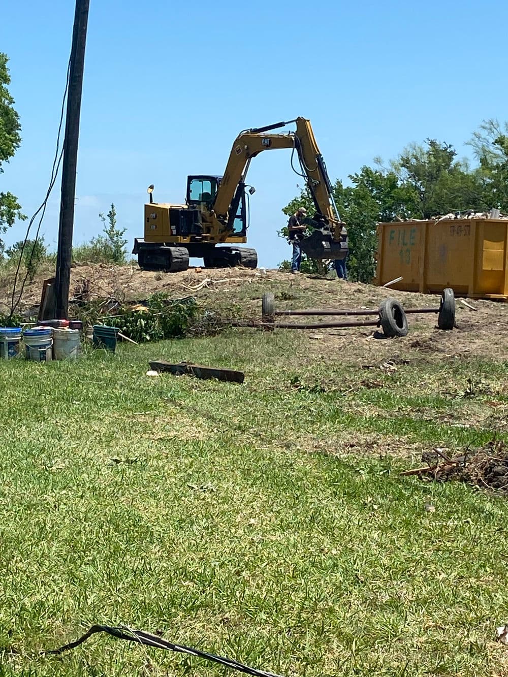 Excavator working on a site with construction debris, tools, and a clear blue sky.
