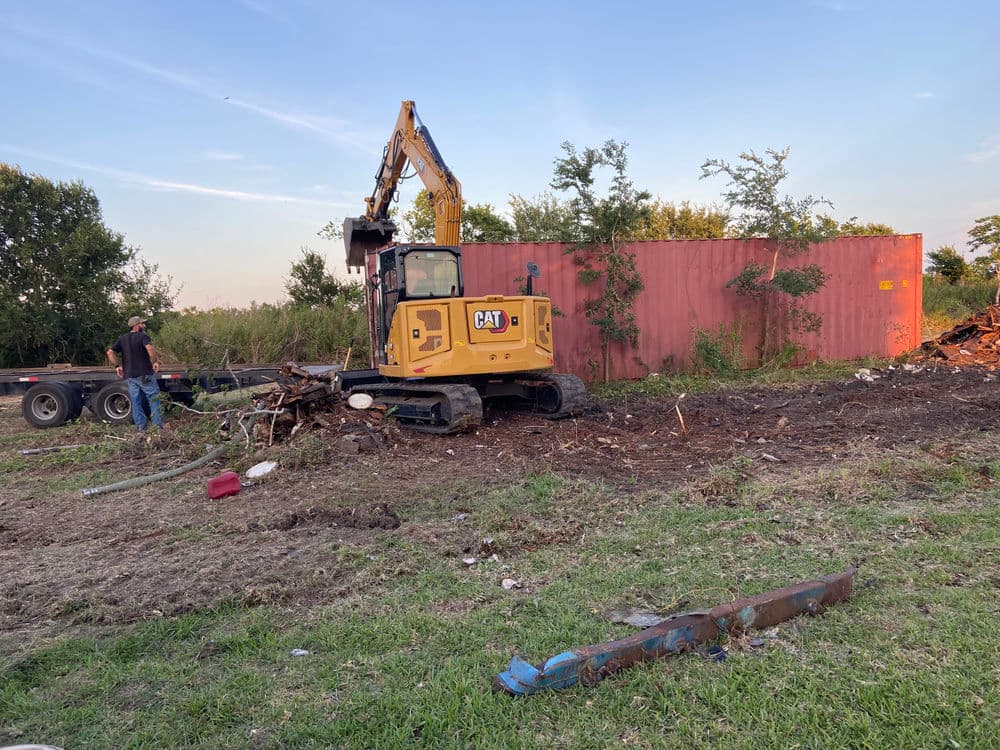 Excavator demolishing debris near a shipping container at a construction site.
