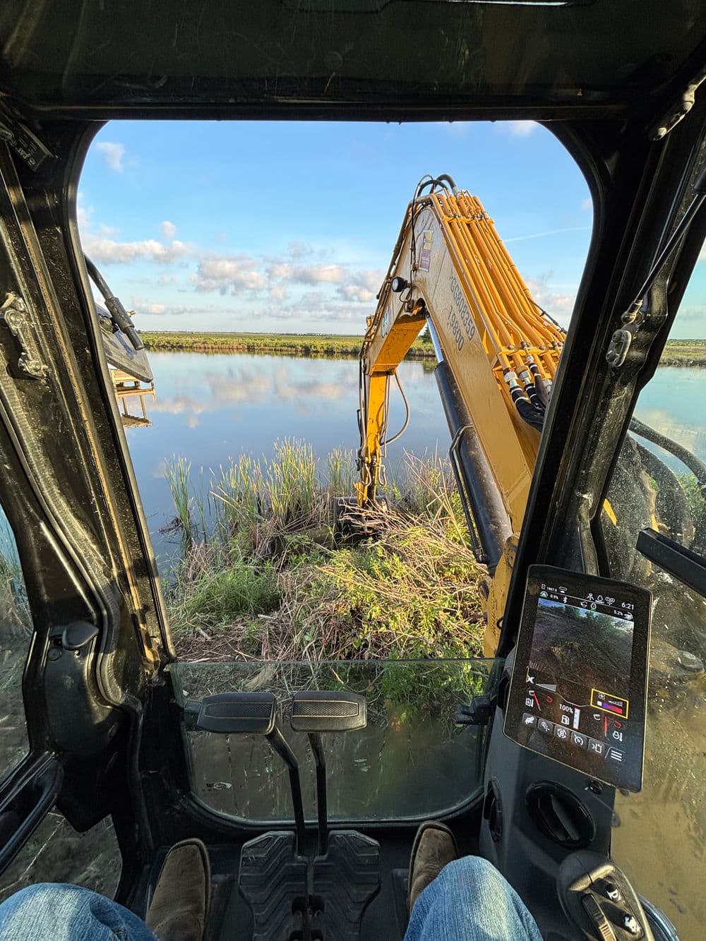 View from an excavator cabin over a marsh, showcasing machinery and natural landscape.