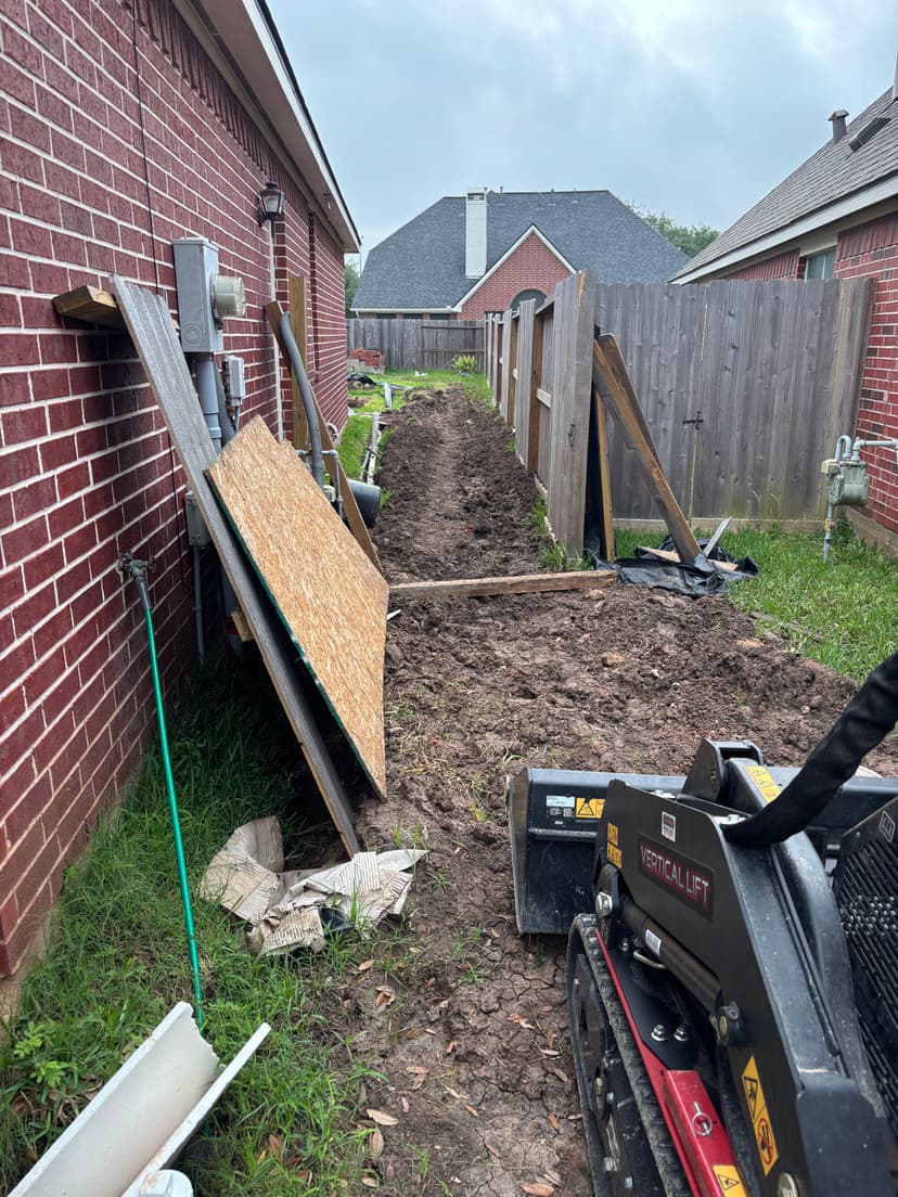 Construction site with a dirt path, equipment, and wooden boards between brick houses.