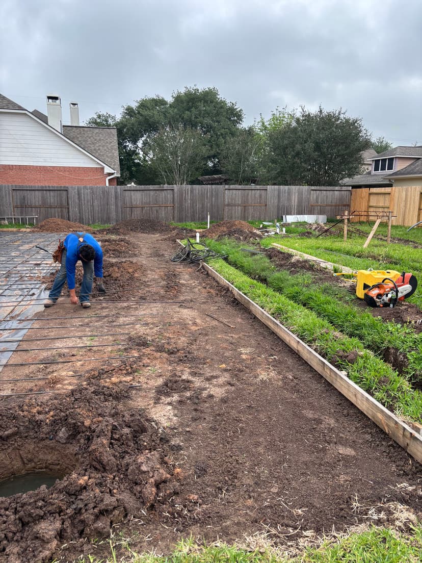 Worker preparing soil for landscaping in a residential garden with leveling tools and grass.